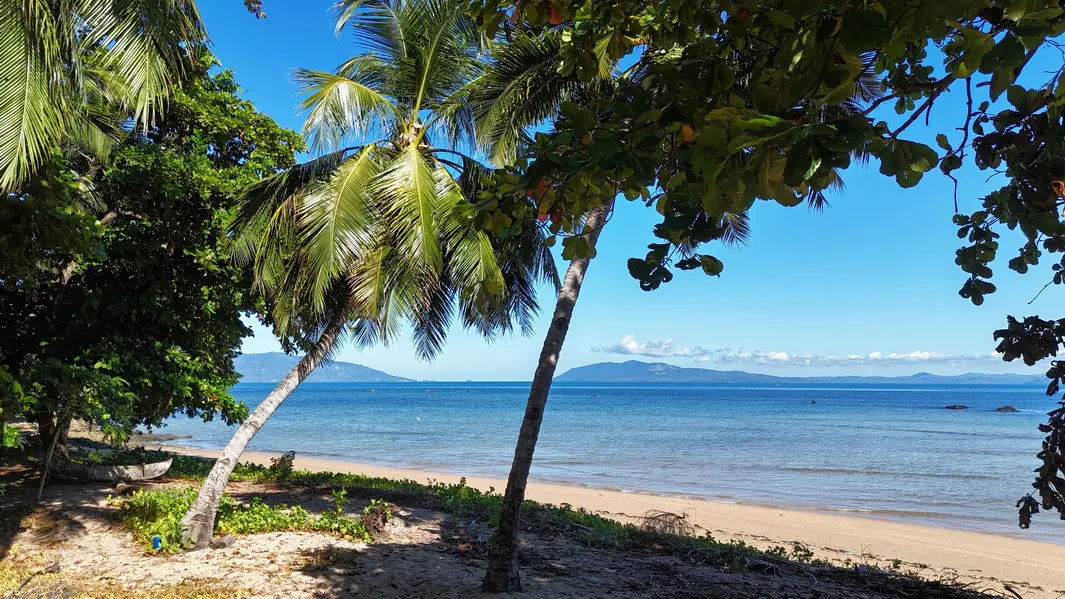 Plage de sable bordant le terrain à vendre à Ampasindava avec cocotiers et vue sur Nosy Komba